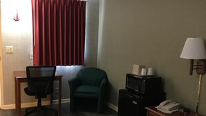 A hotel room with a desk, a green armchair, a microwave, a lamp, and a telephone on a bedside table. - Falls Inn (Newton Falls)