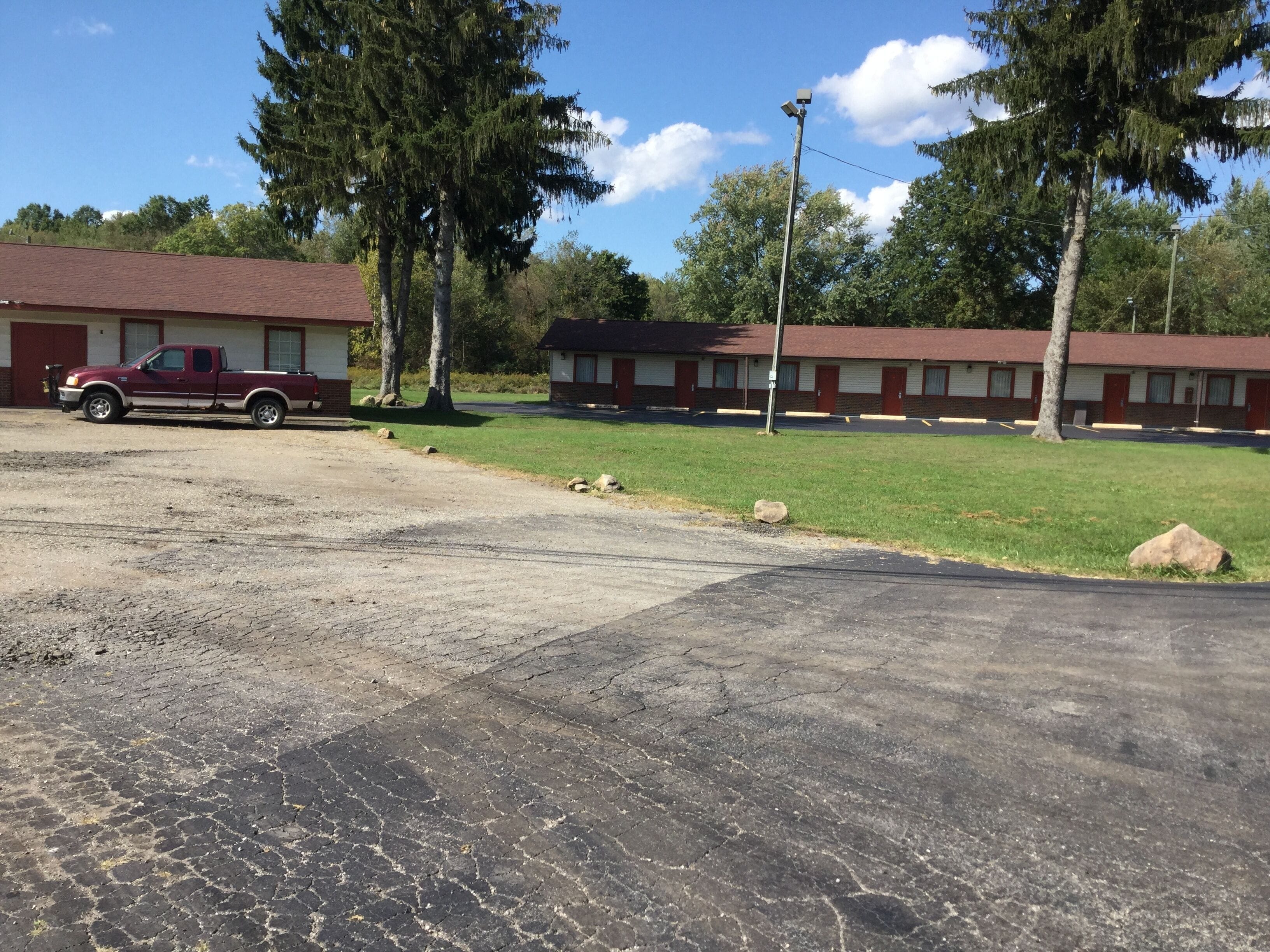 A motel with a red pickup truck parked in the lot, a grassy area, and a building with a brick facade.