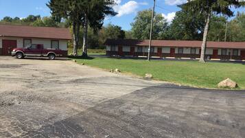 A motel with a red pickup truck parked in the lot, a grassy area, and a building with a brick facade.