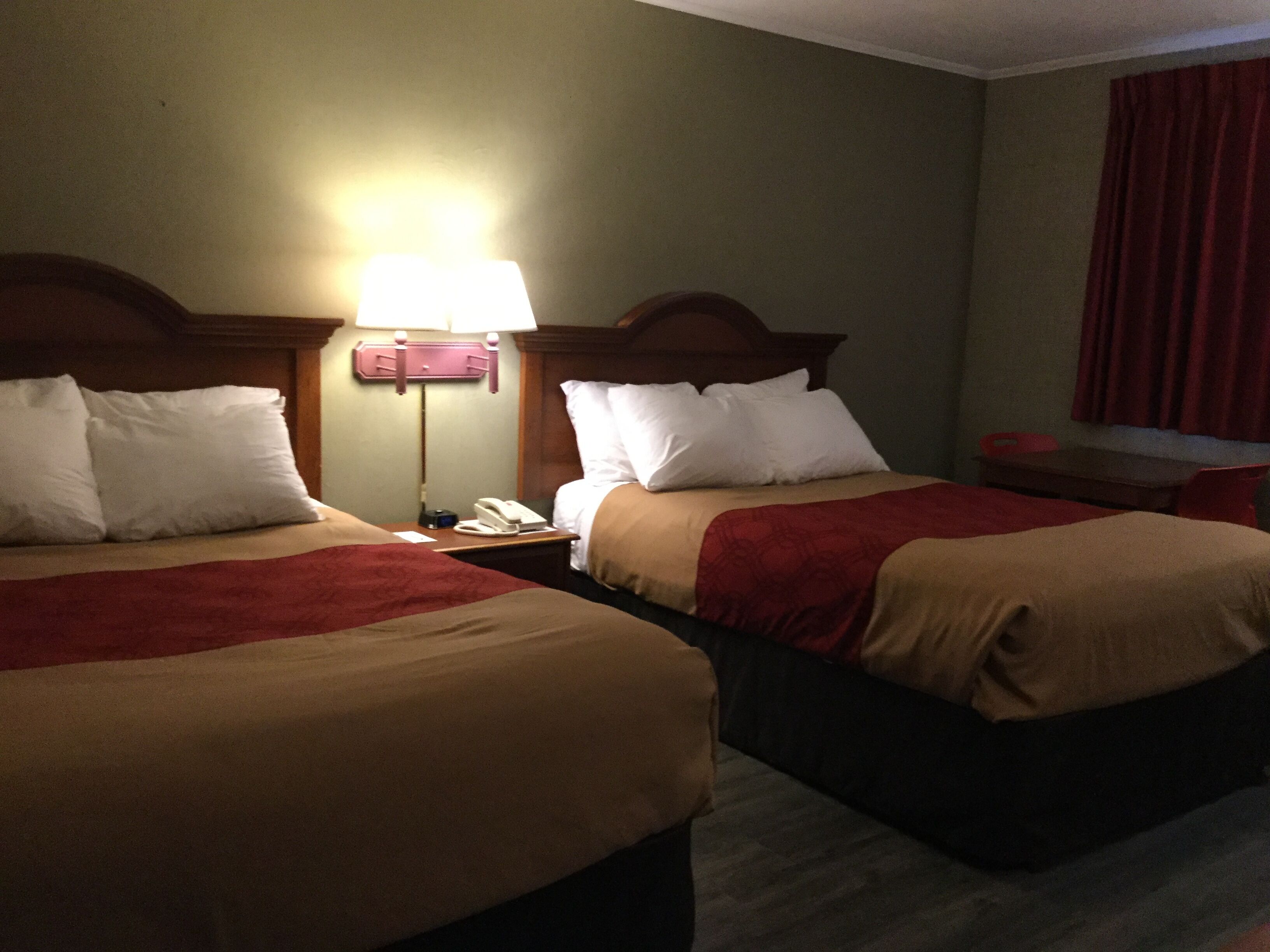 A hotel room with two beds, a nightstand with a lamp, and a desk with a chair.