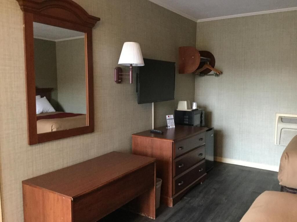 A hotel room with a wooden desk, a television, a mirror, and a coat rack.