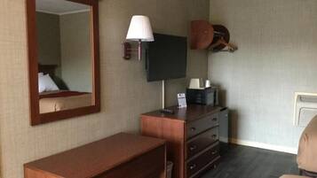 A hotel room with a wooden desk, a television, a mirror, and a coat rack.