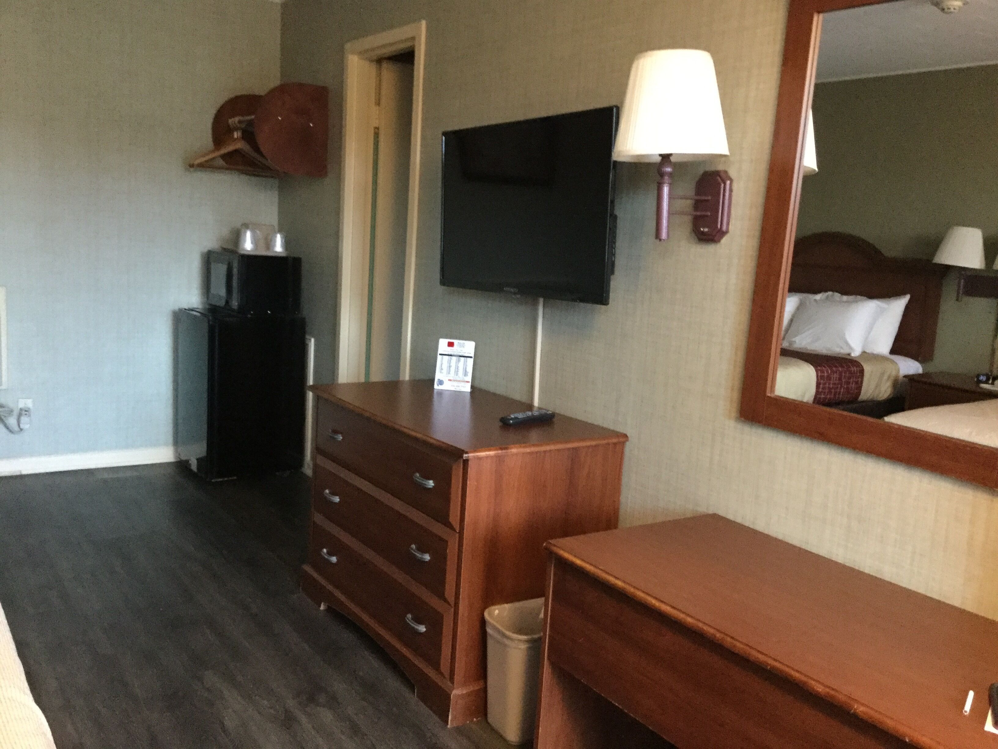 Habitación de hotel con tocador de madera, televisor montado en la pared, espejo y cama con cabecero.