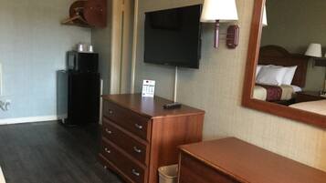 Habitación de hotel con tocador de madera, televisor montado en la pared, espejo y cama con cabecero.