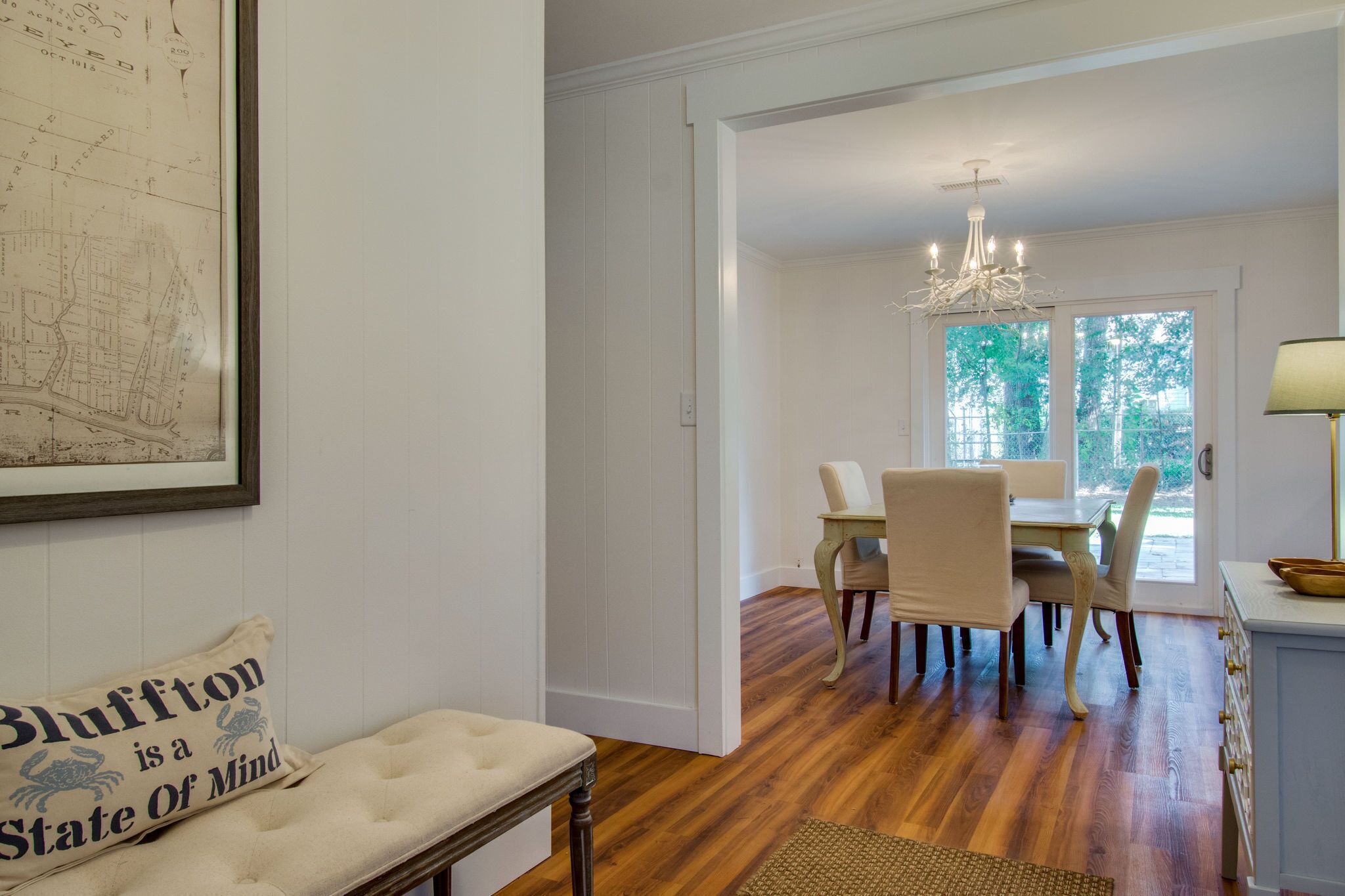 A dining area with a chandelier, wooden flooring, and a view of greenery outside.