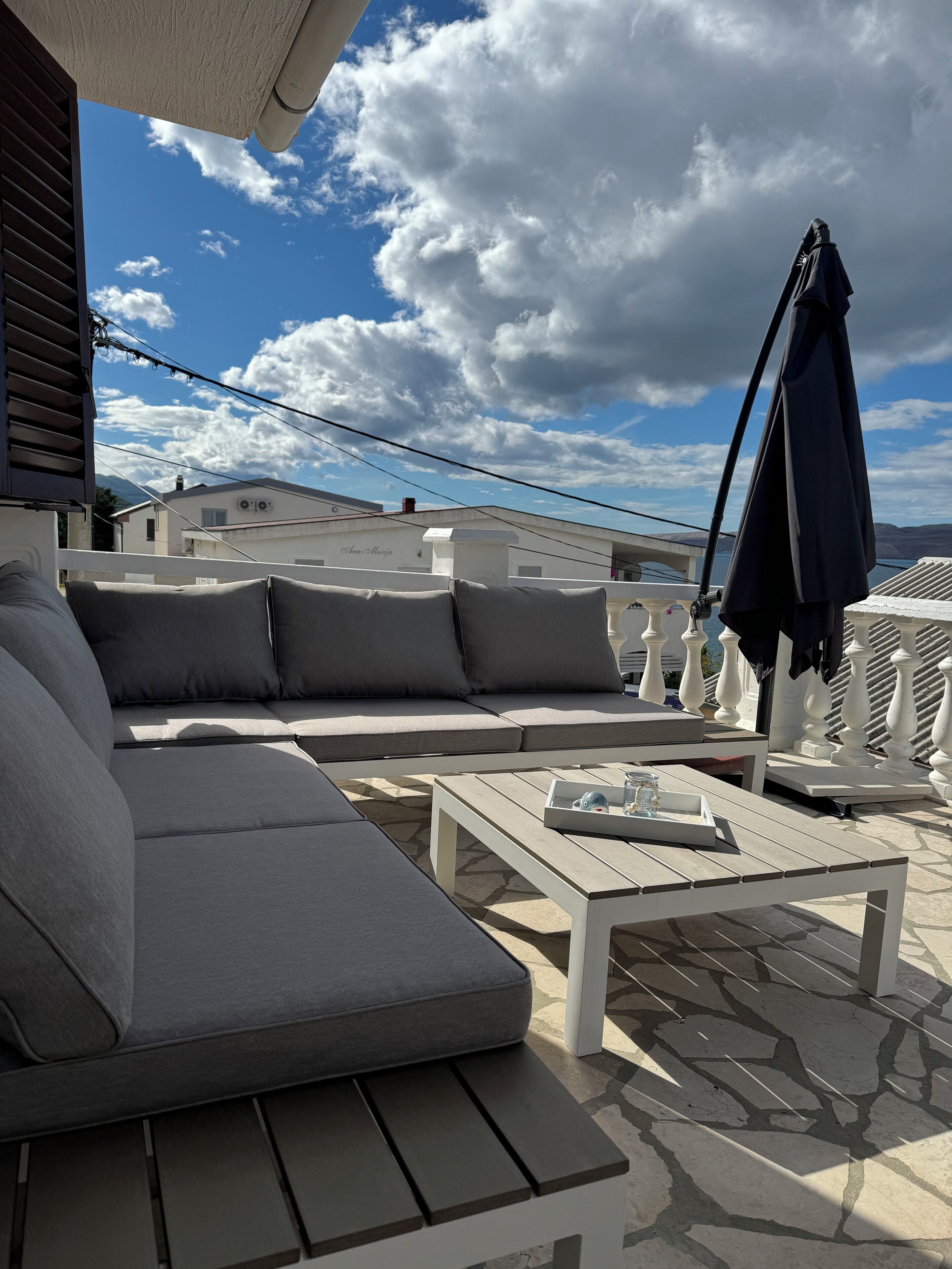 Et moderne udendørs opholdsområde med sofa og bord, hvide gelændere og udsigt til himlen og bygninger i baggrunden.
