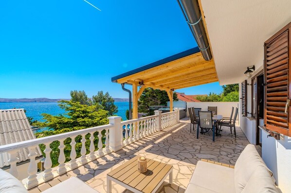 A covered outdoor area with a table and chairs, a view of the sea, and a wooden pergola.