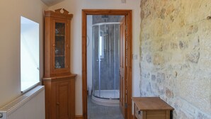 Un couloir avec un radiateur, une armoire en bois, une cabine de douche en verre et un mur en pierre.