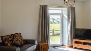 Un salon avec un canapé, un téléviseur posé sur un meuble en bois et une porte donnant sur un espace extérieur verdoyant.