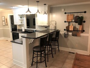 A kitchen with a central island, bar stools, pendant lighting, and a backsplash. - Spacious Country Ranch Home. 25 Private Acres All to Yourself. (Fort Valley)