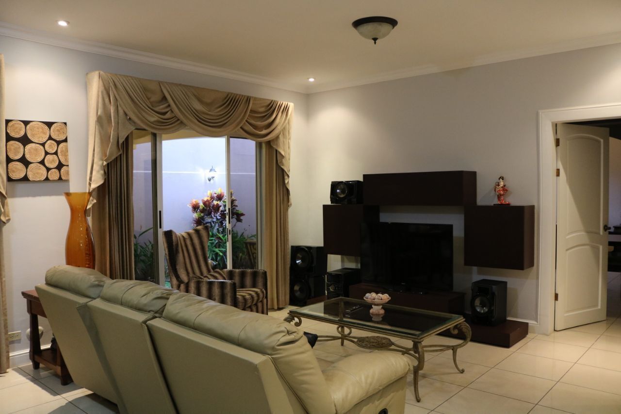 A living room with a beige sofa, a glass coffee table, a fireplace, and a large window with curtains.