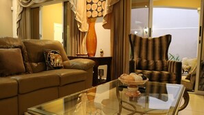 Uma sala de estar com uma mesa de centro de vidro, um sofá marrom e uma poltrona listrada.