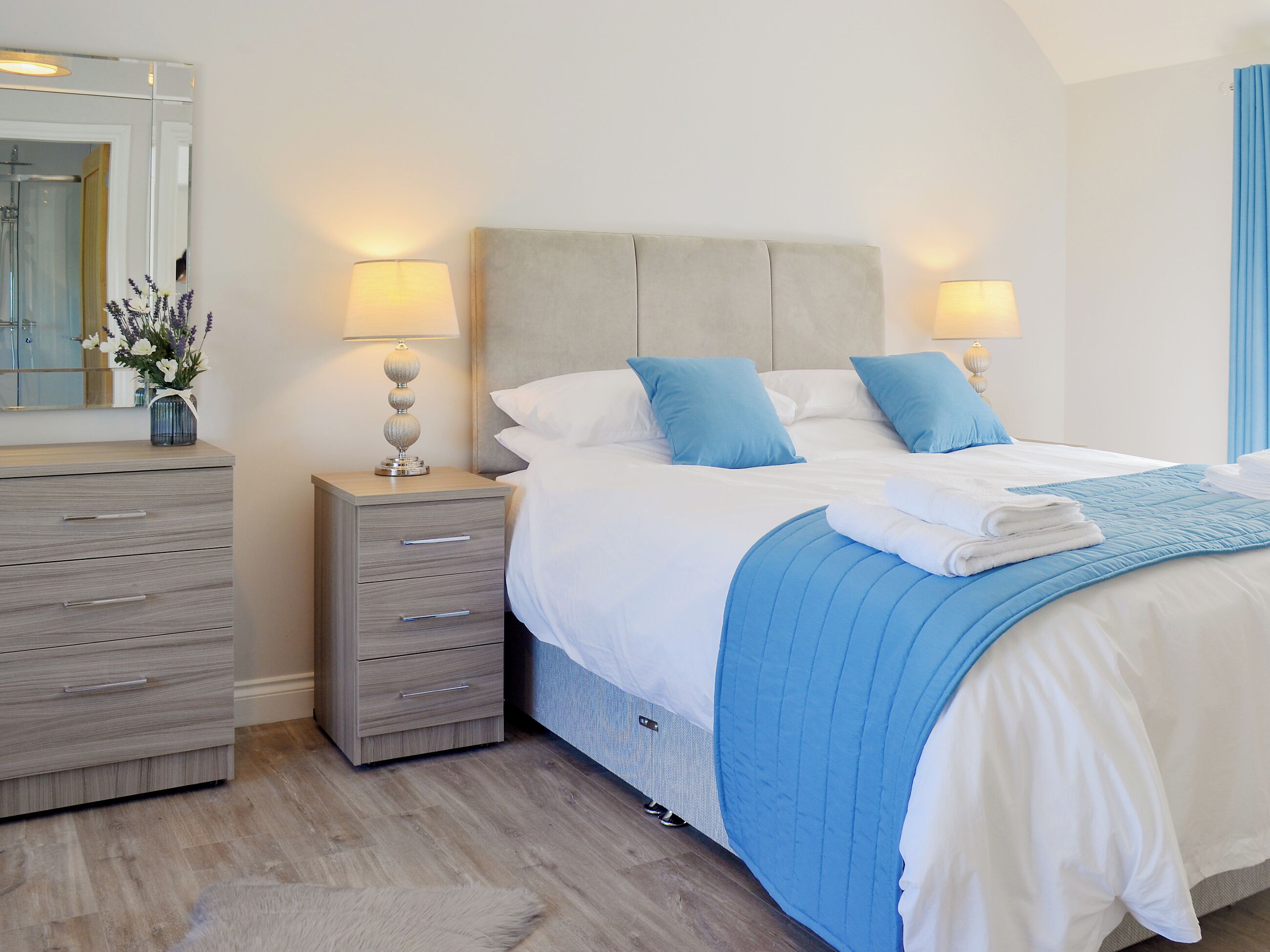 Une chambre à coucher bien rangée, avec un lit, des tables de chevet, une commode et un miroir.