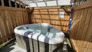 A hot tub in a wooden deck area with a safety sign and a hose.