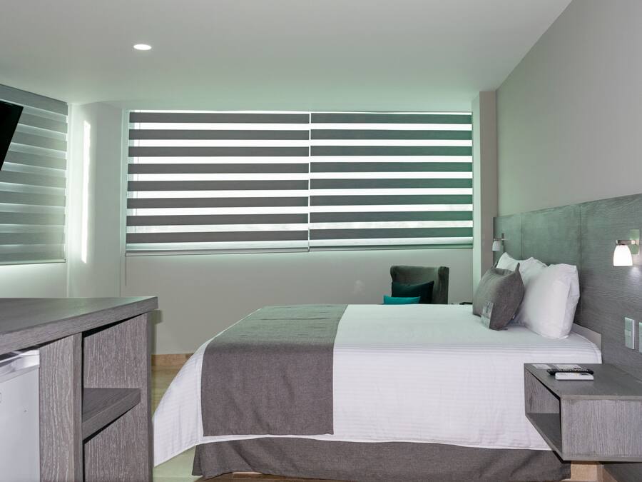 A modern hotel room with a bed, bedside table, and a desk with a chair.