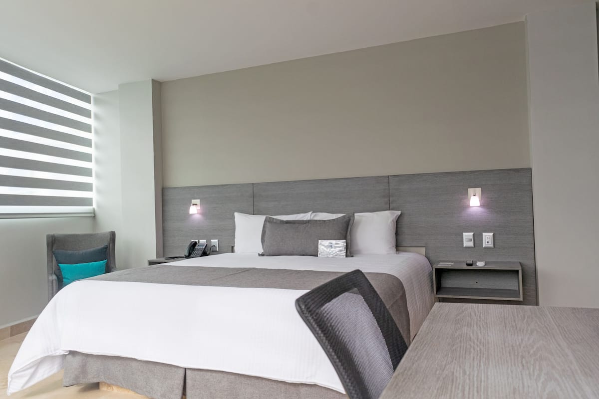 A modern hotel room with a large bed, a desk, and a chair.