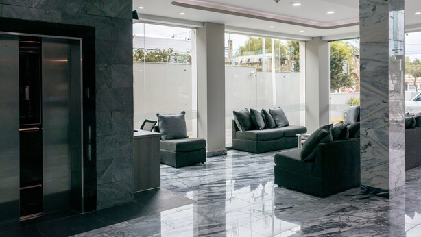 A modern lobby with a marble floor, grey sofas, and a glass elevator. - Hotel 5 Inn Plus (León)