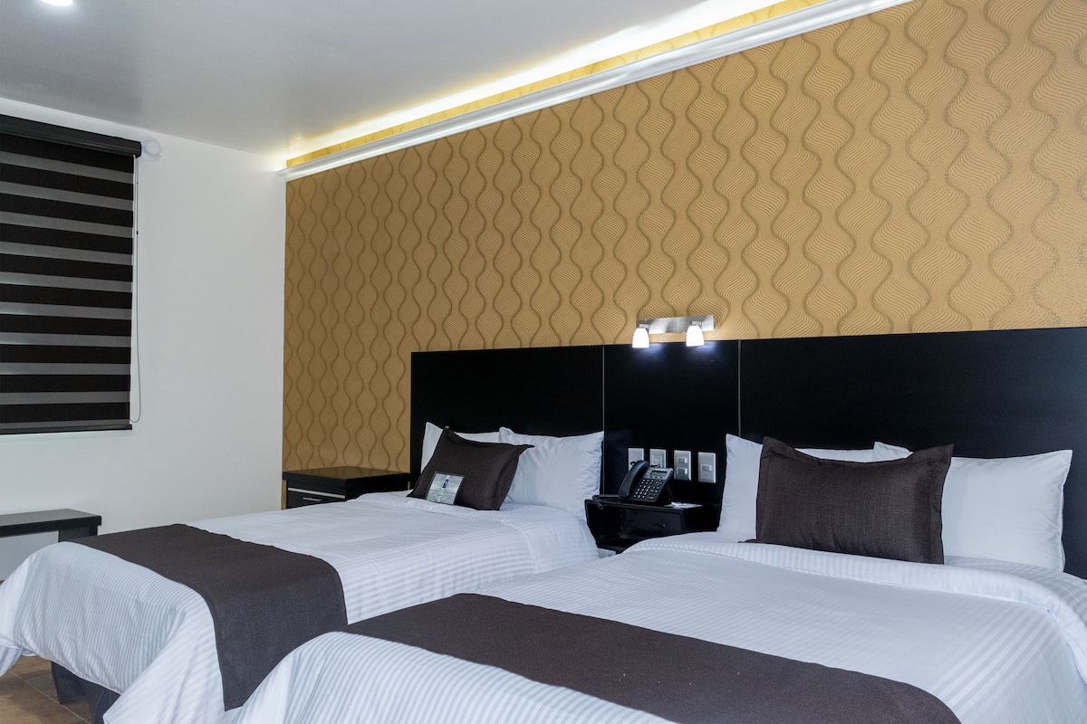 A hotel room with two beds, a headboard with a phone, and a patterned wall.