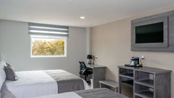 A hotel room with two beds, a desk with a chair, a TV mounted on the wall, and a window with blinds.