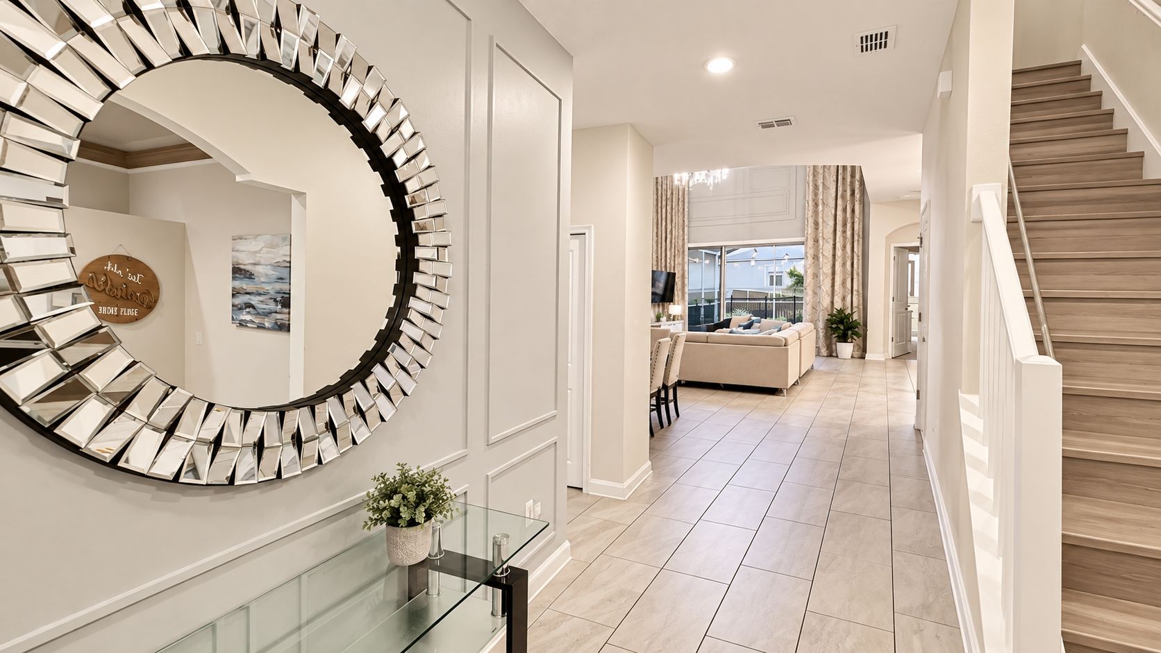 Un couloir moderne avec une table basse en verre, un miroir décoratif et un escalier.