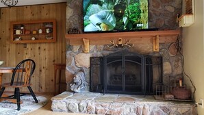 Una chimenea de piedra con un televisor montado encima, una silla de madera y un estante con diversos objetos.