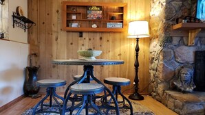 Un interior de madera con una mesa redonda, taburetes, una lámpara y una chimenea de piedra.