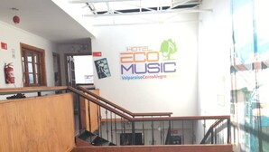 Interior de varios niveles con una escalera de madera, un extintor y una pared con el texto "HOTEL ECO MUSIC Valparaiso Cerro Alegre".