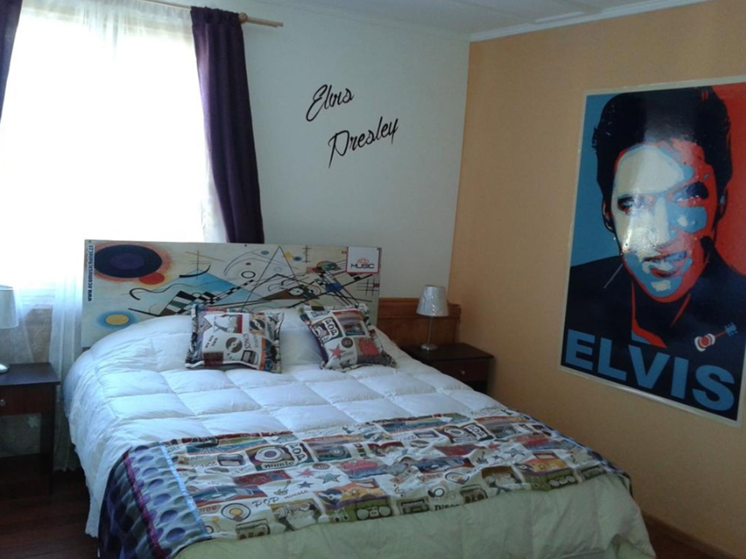A bedroom with a bed, a wall with a poster, and a window with curtains.