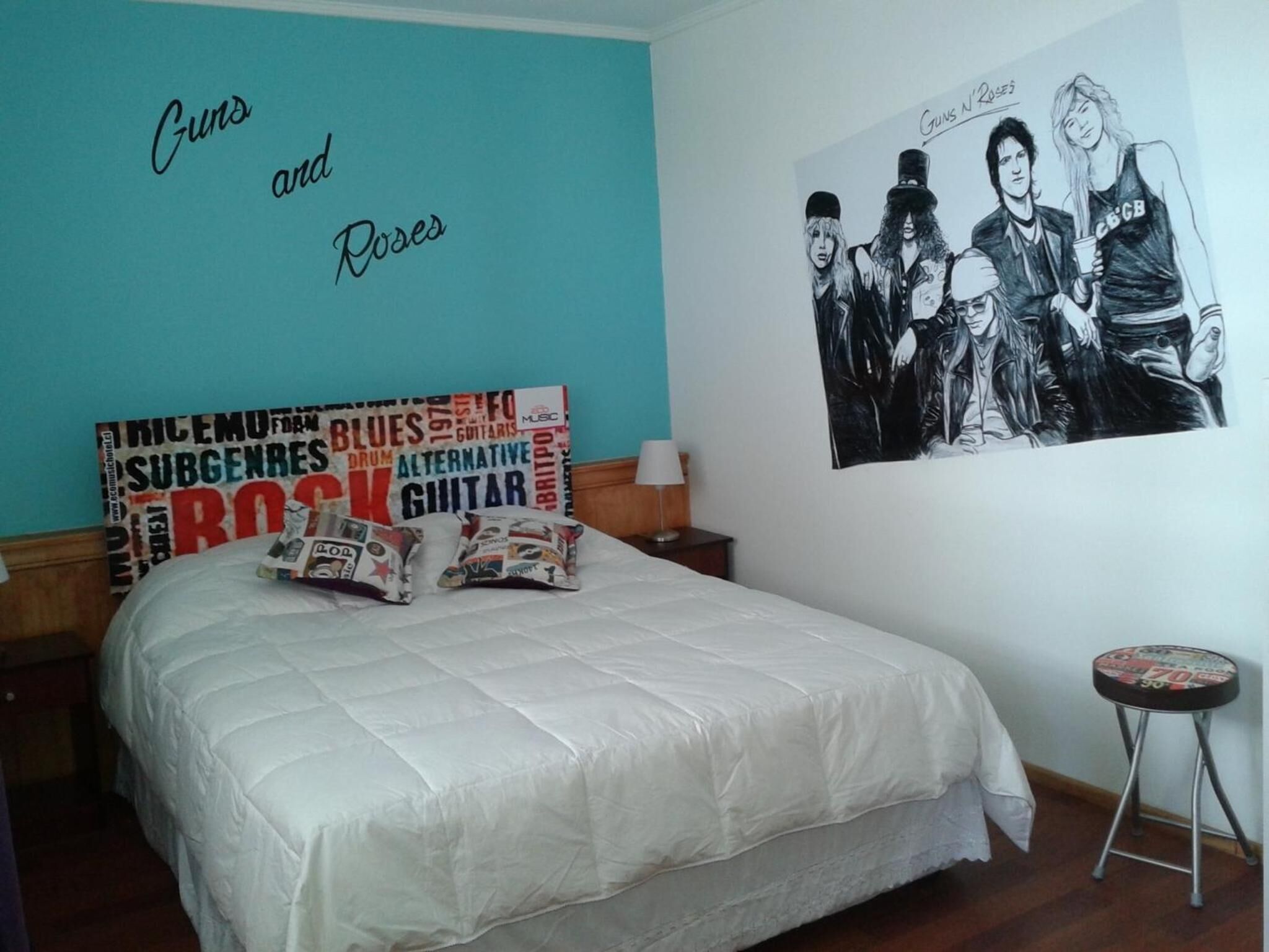 A bedroom with a bed, a wall with a poster, a nightstand, and a small stool.