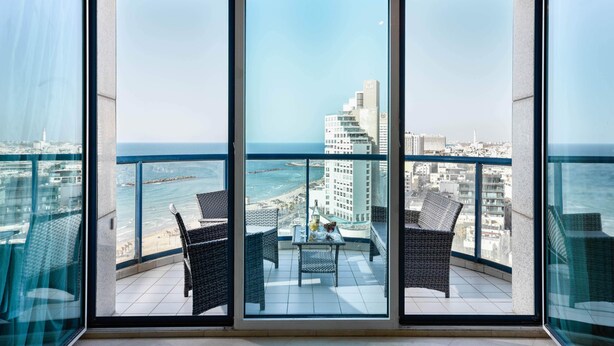 Ein Balkon mit Korbmöbeln, einem Tisch und Blick auf das Meer und die Stadtlandschaft.