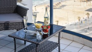 Ein Balkon mit Korbmöbeln, einem Glastisch, einer Champagnerflasche und einer Schale Erdbeeren.