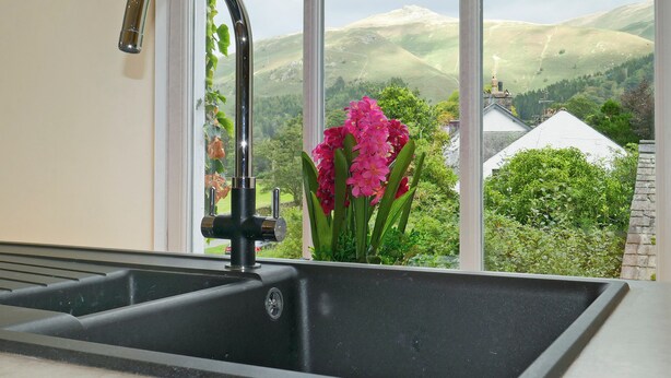 Eine Küchenspüle mit einem modernen Wasserhahn, ein Fenster mit Blick auf grüne Hügel und ein weißes Gebäude.