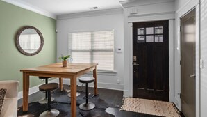 Un coin repas avec une table et des tabourets en bois, une plante en pot et un miroir au mur.