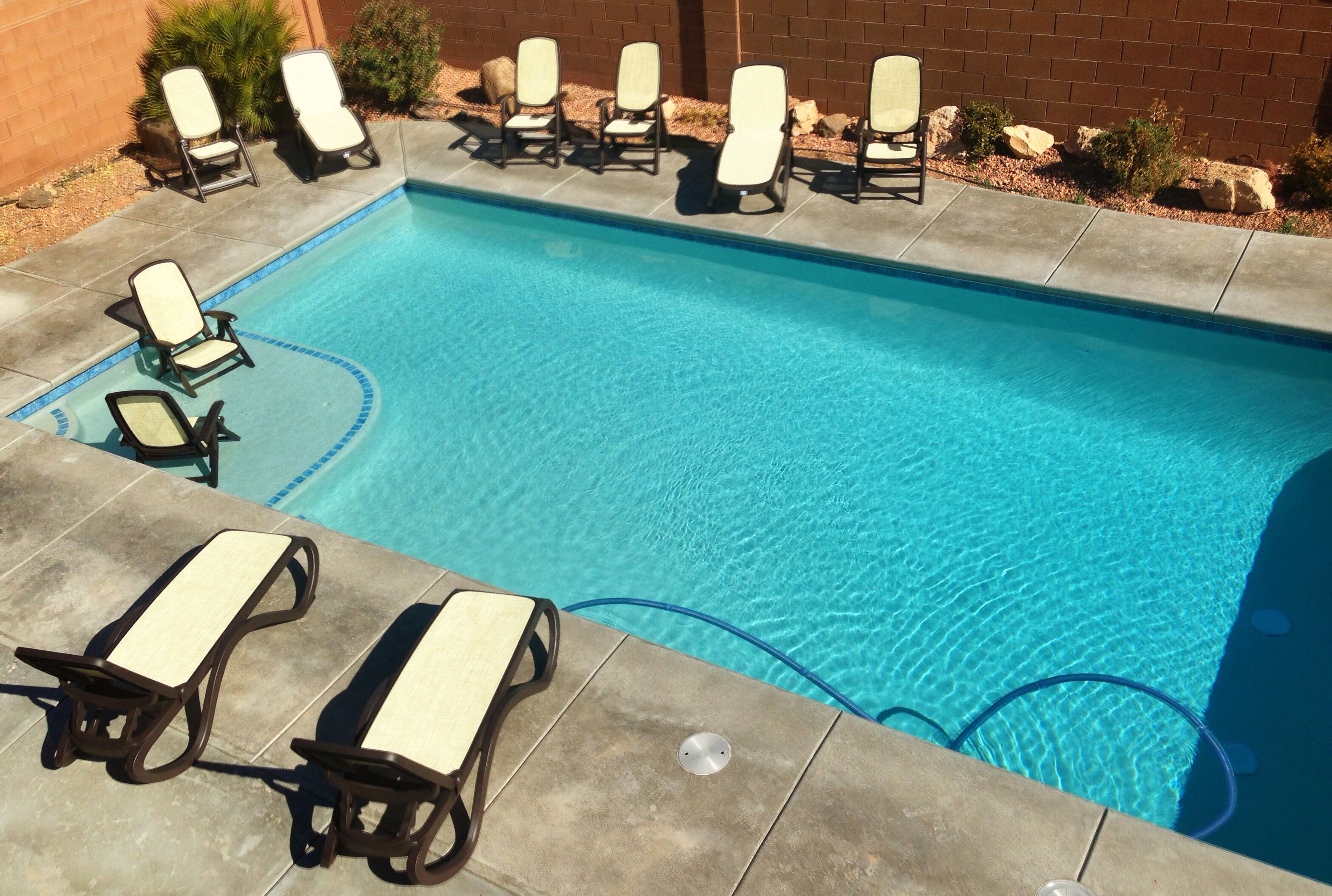 A rectangular pool with clear blue water, surrounded by a tiled deck. There are lounge chairs aligned along the pool's edge.