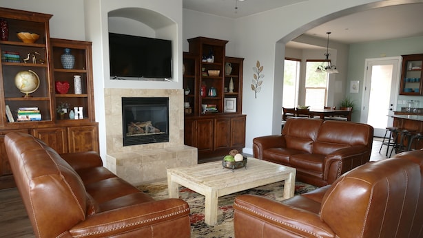 A living room with leather sofas, a fireplace, wooden bookshelves, and a television mounted above the fireplace. - Private Home & Fenced POOL 32'x16', sleeps 15, Jacuzzi,  TV/Game rm, Play-Set (La Verkin)
