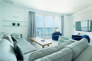 A modern living room with a sofa, a coffee table, and a TV. There is a balcony with a view of the sea. - Luxurious Apt W Panoramic Sea View - 75m (Tel Aviv)