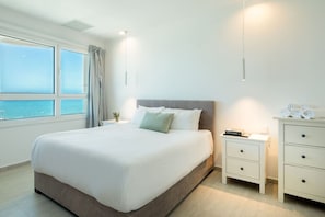 Une chambre à coucher avec un grand lit, une table de chevet, une commode et une fenêtre donnant sur la mer.