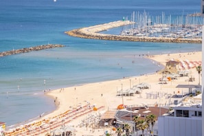A beach with a rocky breakwater, a marina with sailboats, and beach umbrellas. - Luxurious Apt W Panoramic Sea View - 75m (Tel Aviv)