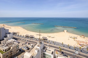 A coastal cityscape with a beach, clear blue sea, and urban buildings. - Luxurious Apt W Panoramic Sea View - 75m (Tel Aviv)