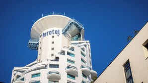 Een modern hotel met een opvallend rond dak, balkons en een helderblauwe lucht.