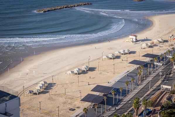 A beach with a lifeguard tower, umbrellas, and a road with palm trees.