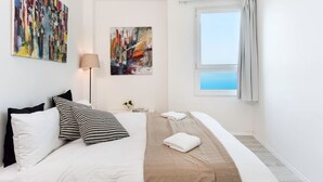 A hotel room with a bed, two paintings, a window with curtains, and a view of the sea. - Luxurious 90sqm 2BR Beach Front (Tel Aviv)