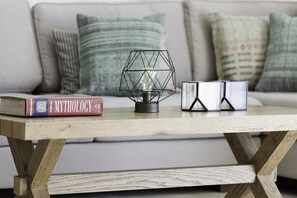 A wooden table with a geometric light fixture, a book titled 'MYTHOLOGY', and two glass candle holders.