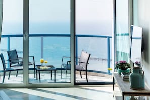 A balcony with a view of the sea, furnished with chairs and a table, and a vase with flowers.