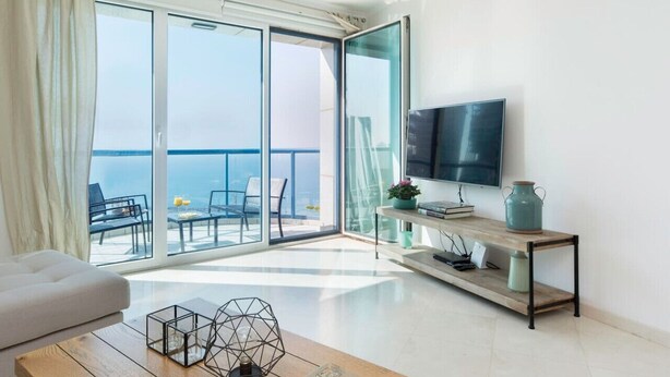 A modern living room with a large sliding glass door leading to a balcony with a view of the sea. - Luxurious 90sqm 2BR Beach Front (Tel Aviv)