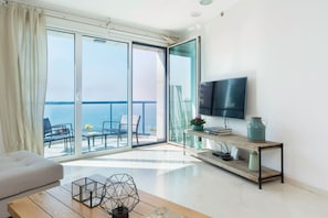 Un salon moderne avec un téléviseur, un canapé, une table basse et un balcon offrant une vue sur la mer.