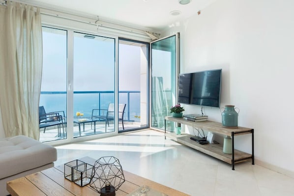 Un salon moderne avec un téléviseur, un canapé, une table basse et un balcon offrant une vue sur la mer.