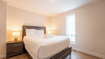 A bedroom with a wooden bed, two bedside tables with lamps, a window, and a light switch on the wall.