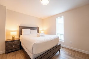 Une chambre à coucher avec un lit en bois, deux tables de chevet avec des lampes, une fenêtre et un interrupteur sur le mur.