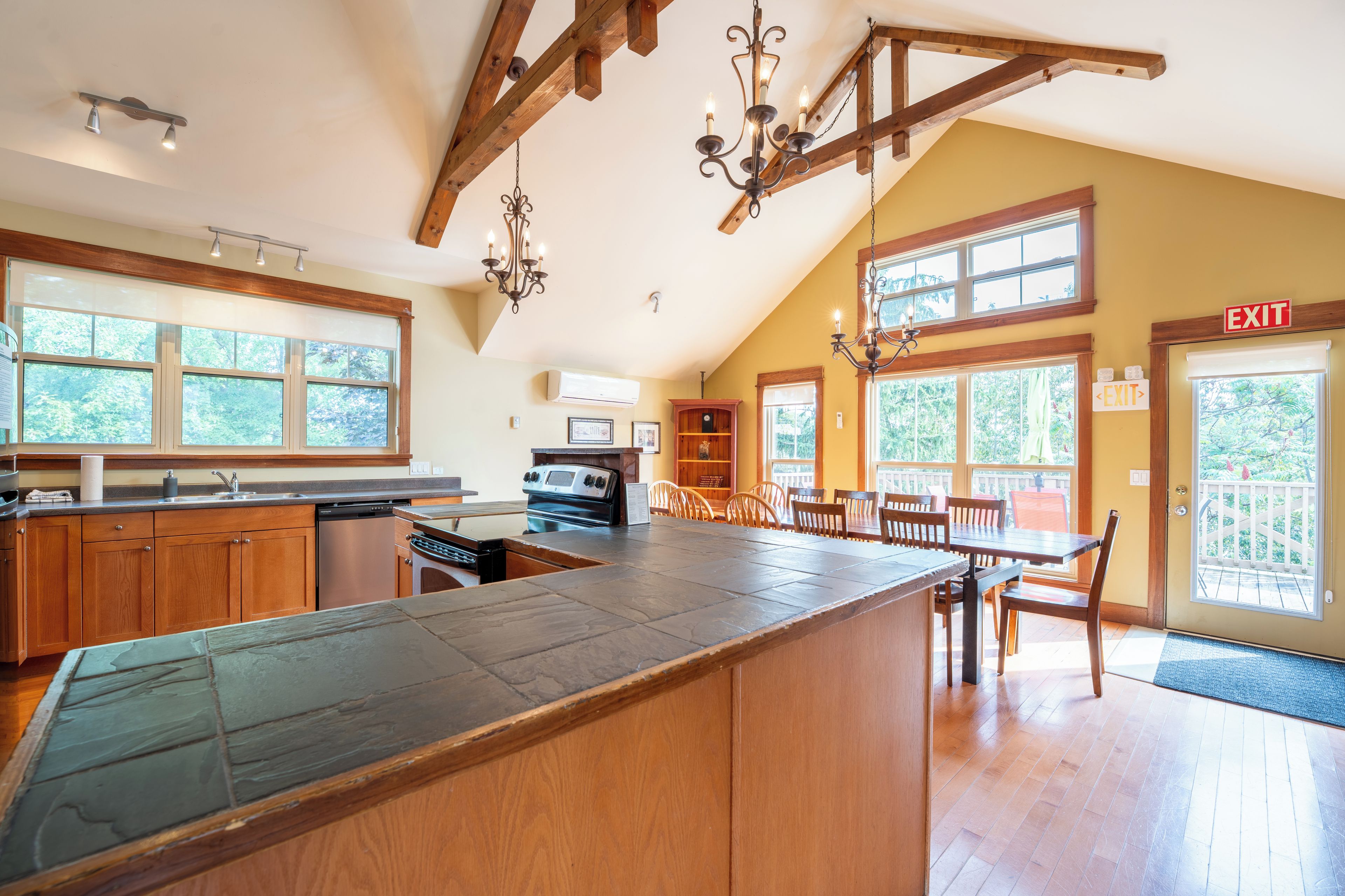 A spacious kitchen with wooden cabinets, a large island, and a dining area with a high ceiling and wooden beams.